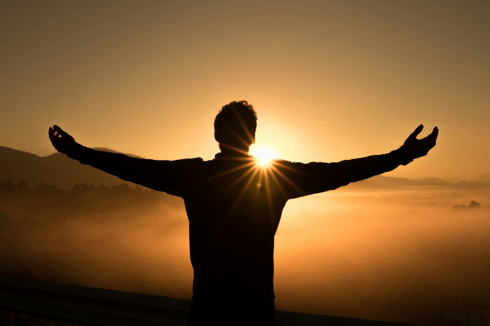 Person greeting the sunrise with open arms above misty hills — hope and recovery from anxiety and depression in West Virginia
